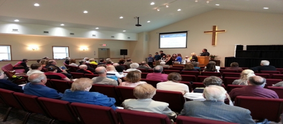 The congregation seated for worship, facing a wooden cross on the front wall